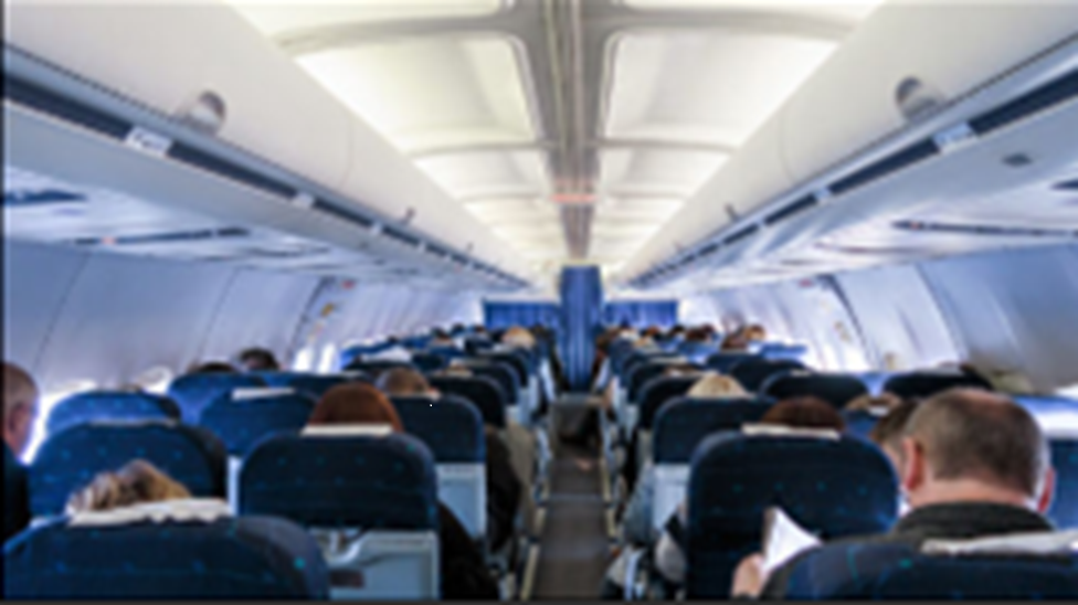 A long view, down the center of the cabin of a passenger airplane, with passengers seated on both the left and the right.